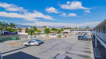 Un parking avec plusieurs voitures, un immeuble doté d’un balcon et des montagnes en arrière-plan.