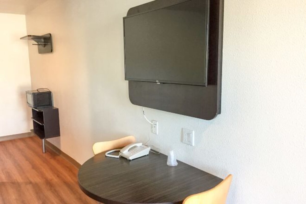 A small room with a dark wooden table, two chairs, a white telephone, and a mounted flat-screen TV.