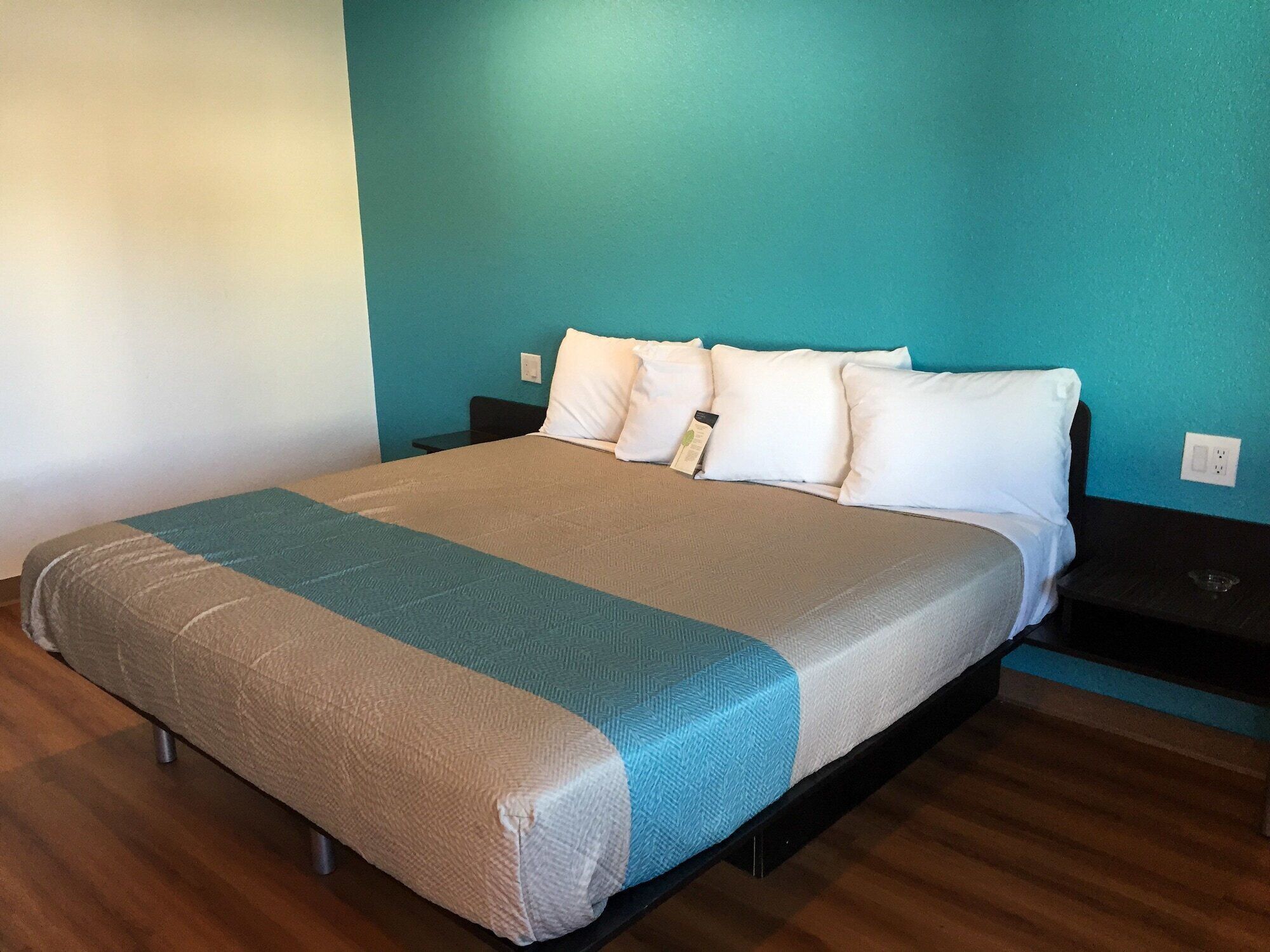 A neatly made bed with a beige and teal bedspread, white pillows, and a black nightstand with a small table beside it.