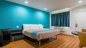 Une chambre d’hôtel avec un lit, un bureau, une chaise, un radiateur et une porte.