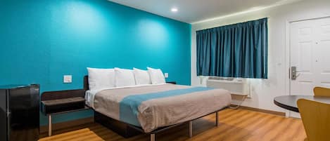 A hotel room with a bed, a desk, a chair, a heater, and a door.