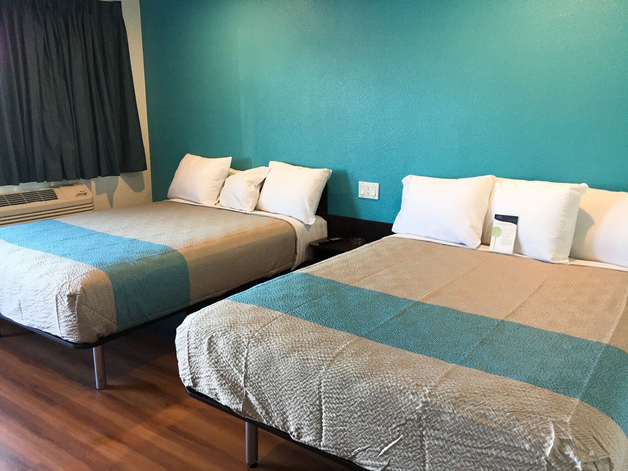 Two single beds with matching headboards and footboards, a bedside table, and a wall-mounted air conditioning unit.
