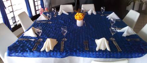 A dining table set with white chairs, a blue tablecloth, and a vase of yellow flowers.