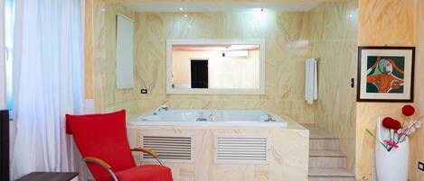 A modern bathroom with a large bathtub, a red chair, and a framed artwork on the wall.