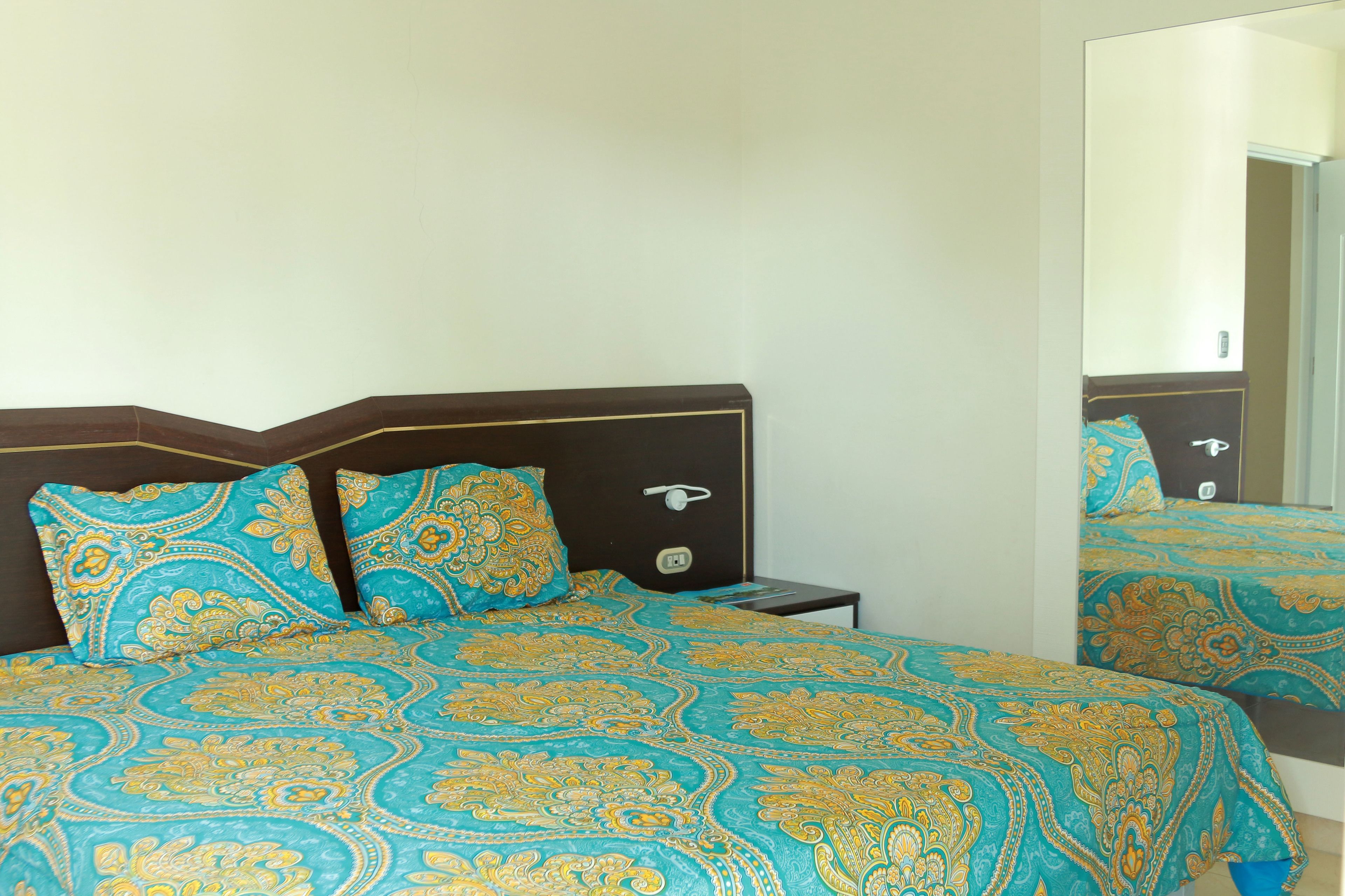 Een slaapkamer met een bed, twee kussens, een nachtkastje en een spiegel.