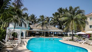 A swimming pool with lounge chairs, palm trees, and a building in the background. - Kitewind Apartahotel Cabarete (Cabarete)