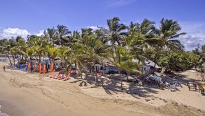 A beach with rows of sun loungers and palm trees, a beach hut, and a few people walking. - Kitewind Apartahotel Cabarete (Cabarete)