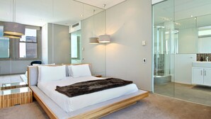 A modern bedroom with a large bed, bedside tables, a mirror, and a glass shower enclosure.