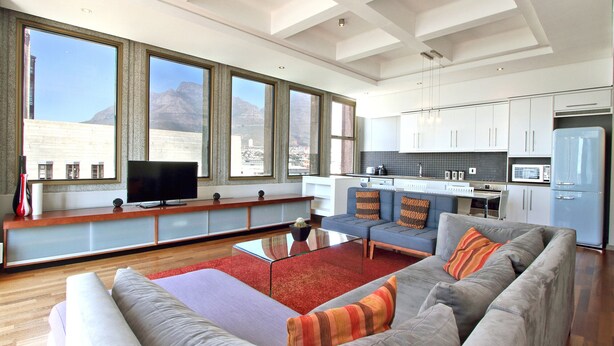 A modern living room with a grey sofa, red rug, and a flat-screen TV.