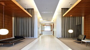 A modern hotel lobby with a long corridor, wooden paneling, a bench, a sofa, and a chair.
