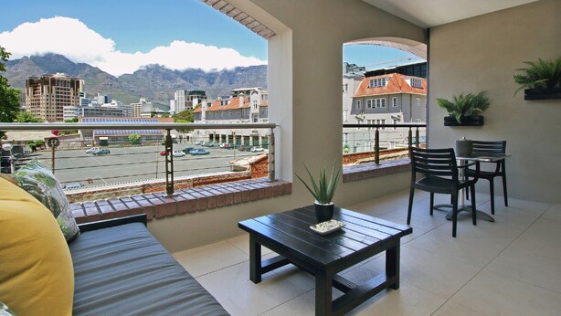 A balcony with a view of a cityscape and mountains. There is a sofa, a table with a plant, and two chairs. - ITC Hospitality Group One Bedrooms Rockwell Building (Cape Town)