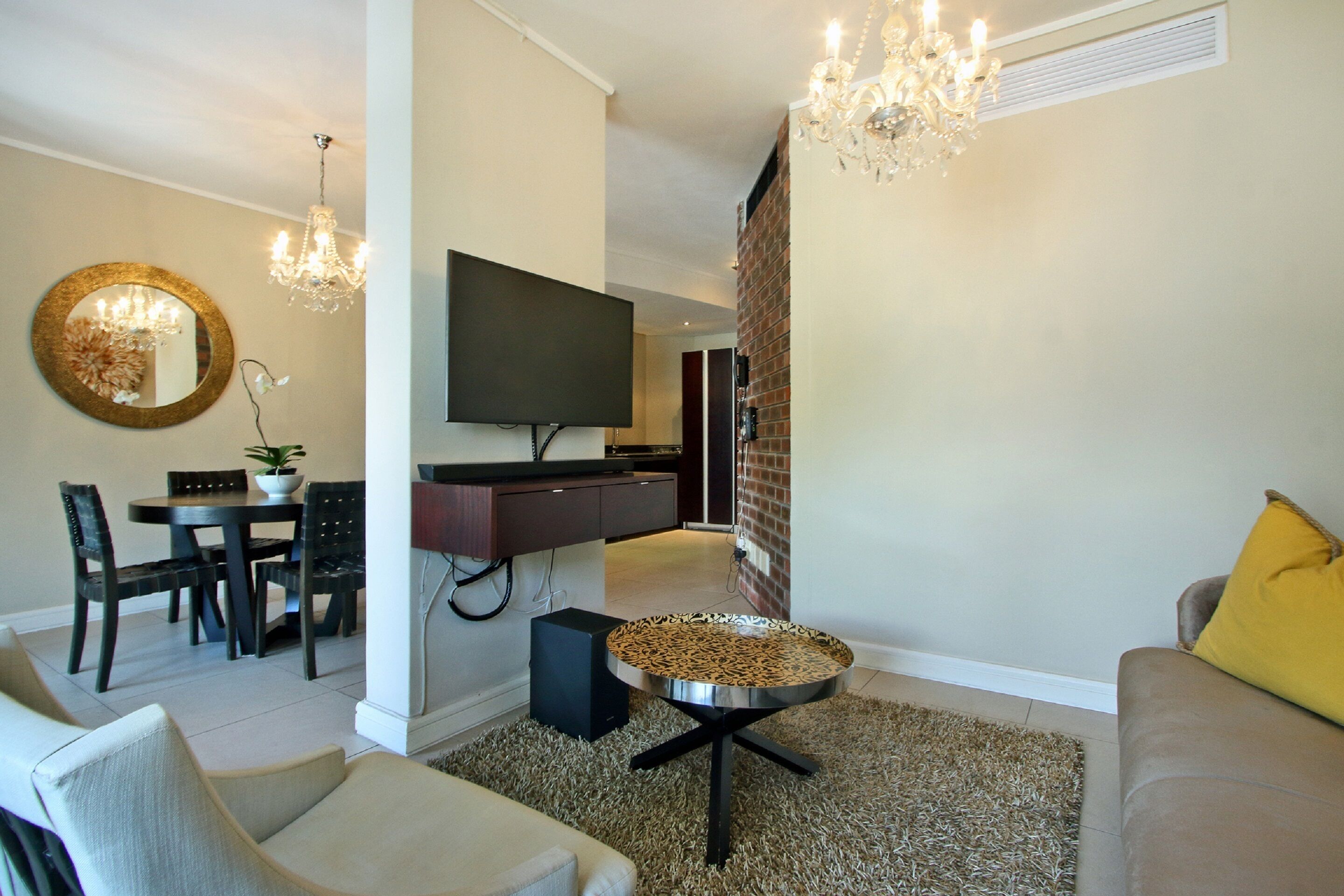 A modern living room with a flat-screen TV, dining table, chairs, and a coffee table.