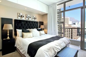 Een moderne slaapkamer met een groot bed, twee nachtkastjes en uitzicht op de stad door grote ramen.