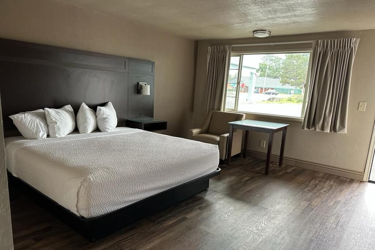 Een hotelkamer met een groot bed, een klein tafeltje, een stoel en een raam met gordijnen.