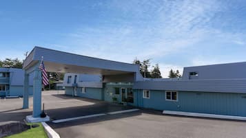 A motel with a covered parking area, a flagpole with an American flag, and a clear blue sky.