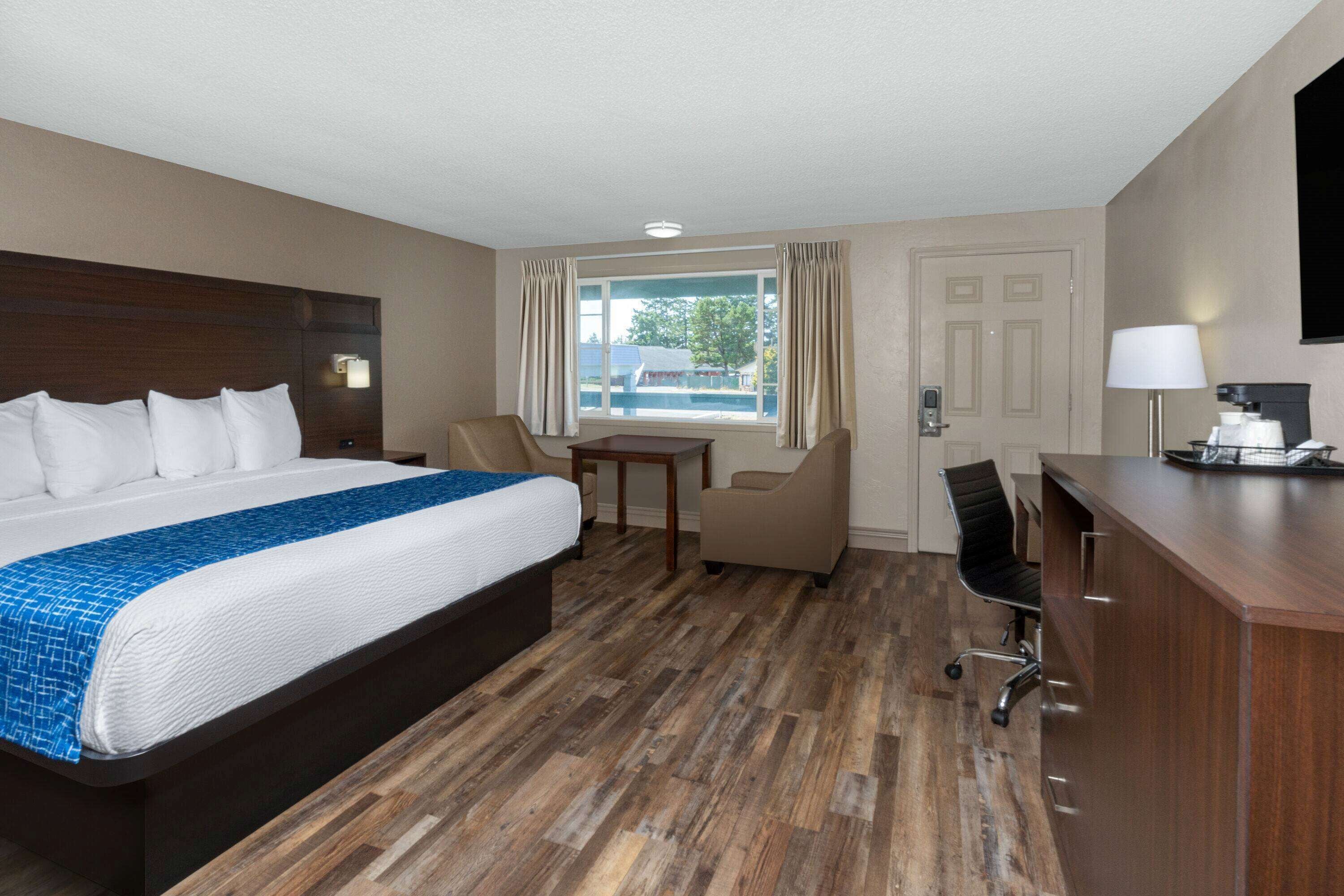 A hotel room with a large bed, a desk, a chair, a TV, and a window with curtains.