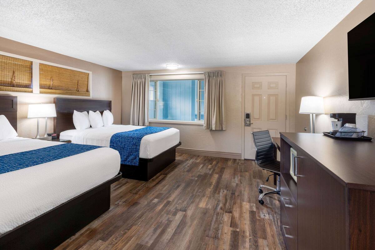 Een hotelkamer met twee bedden, een bureau, een stoel, een televisie en een raam met gordijnen.