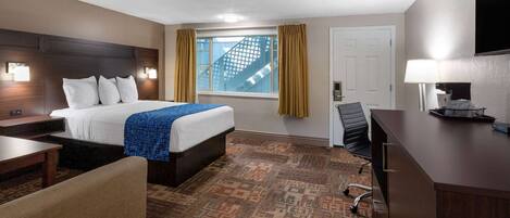 A hotel room with a large bed, a desk, a chair, a desk lamp, and a window with curtains.