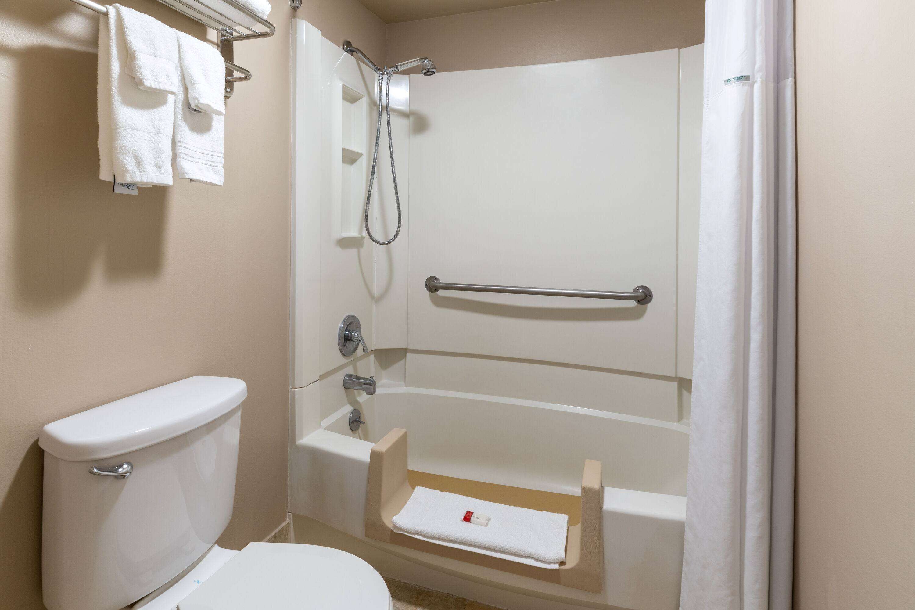 A bathroom with a toilet, a shower with a grab bar, and a towel rack with towels.
