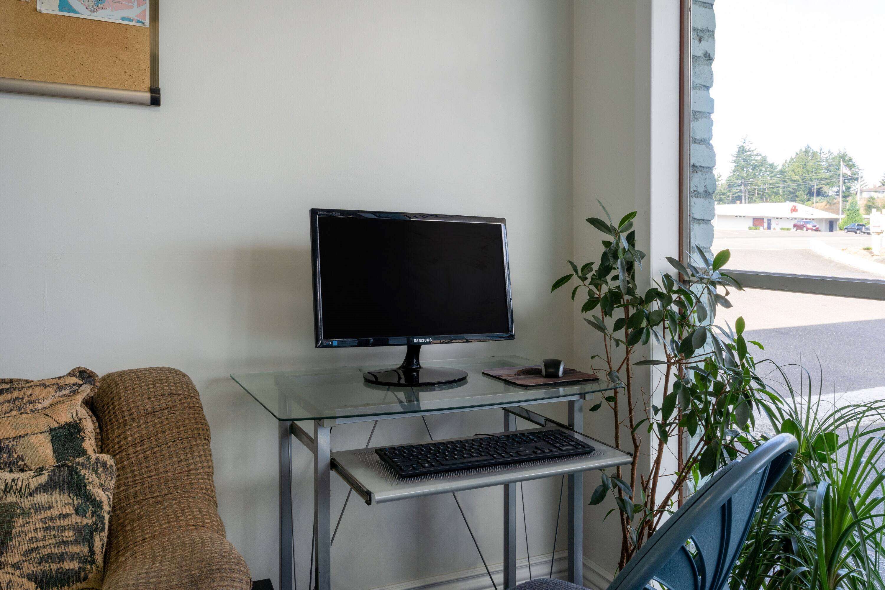 A modern office space with a glass desk, a computer monitor, keyboard, and a cushioned chair.
