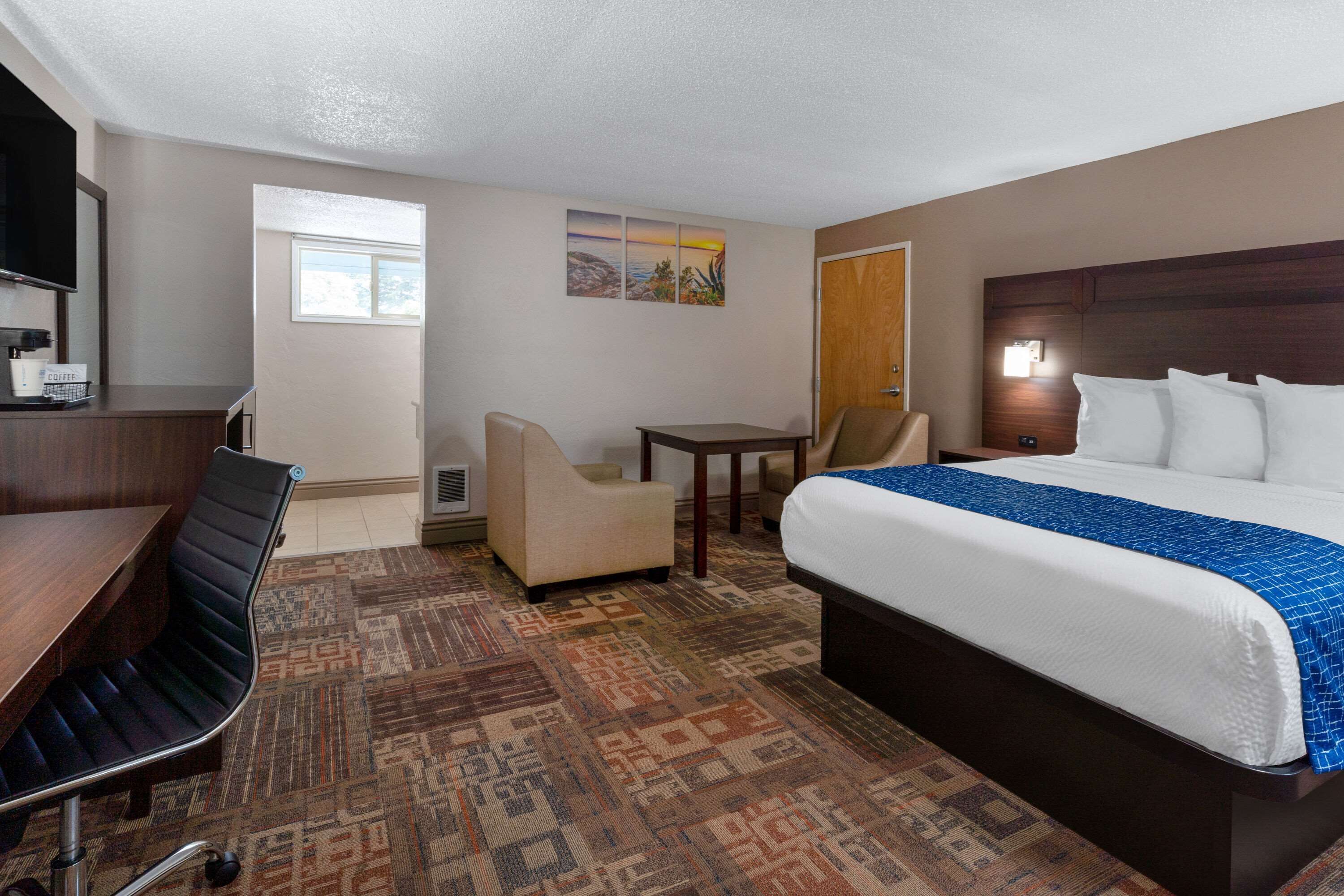 Una habitación de hotel con cama, escritorio, silla, mesita y ventana.