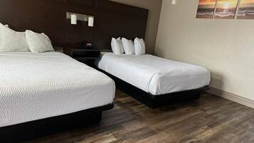 Una habitación de hotel con dos camas, piso de madera, una mesita de noche y una lámpara fijada a la pared.