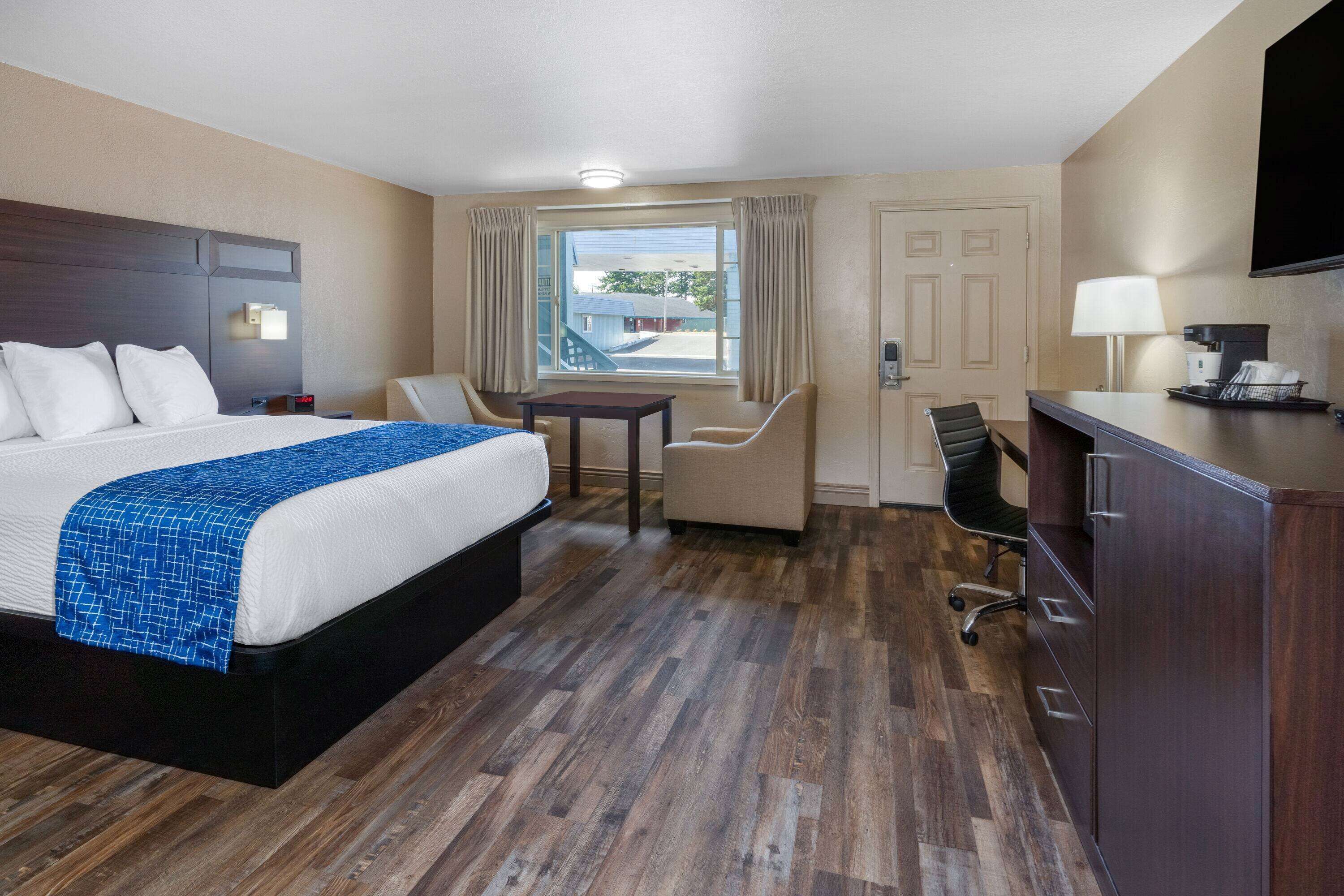 A hotel room with a bed, a desk, a chair, a TV, and a window with curtains.
