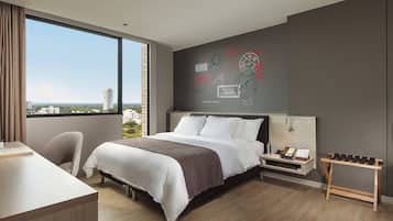A modern hotel room with a large bed, a desk, and a view of the city.
