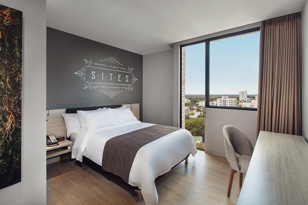 A modern hotel room with a large bed, a desk, and a view of the city.