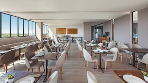 A modern dining area with multiple tables and chairs, large windows offering a view of the outdoors, and a minimalist interior design. - Hotel Sites Monteria (Montería)