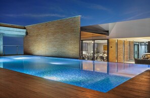 An infinity pool with a wooden deck, a brick wall, and a modern interior with glass doors and a dining area. - Hotel Sites Monteria (Montería)