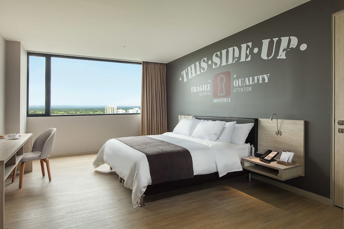 A modern hotel room with a large bed, a desk, and a view of the city.