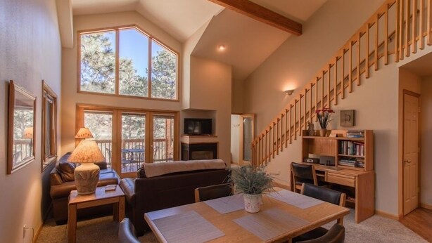 A spacious living area with a high ceiling, large windows, a wooden staircase, and a cozy seating arrangement. - Riverwood on Fall River (Estes Park)
