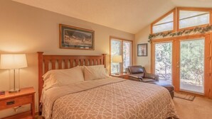 A bedroom with a large bed, a nightstand, a chair, and a window with blinds. - Riverwood on Fall River (Estes Park)