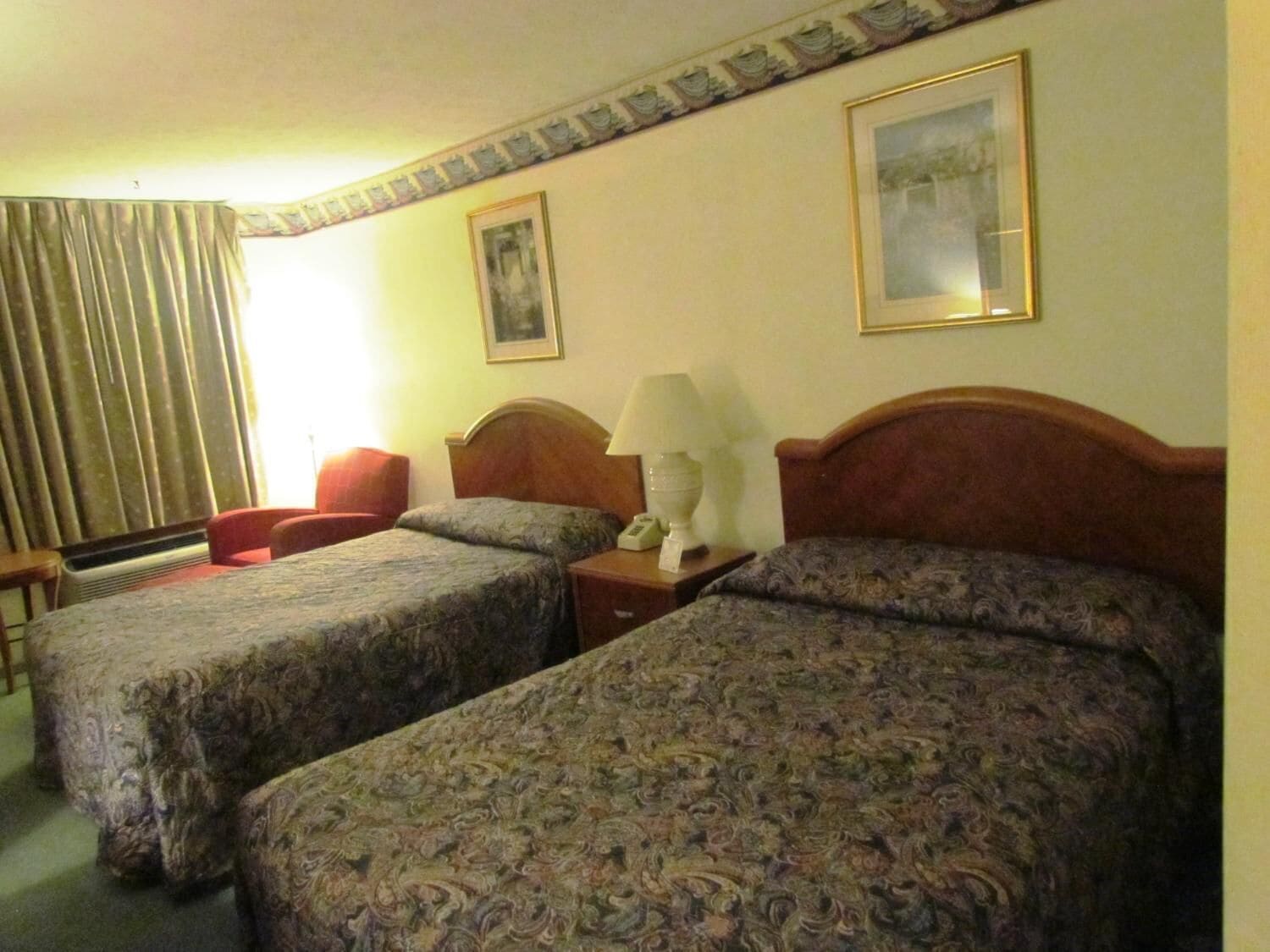 A hotel room with two beds, a desk, a chair, and a window with curtains.