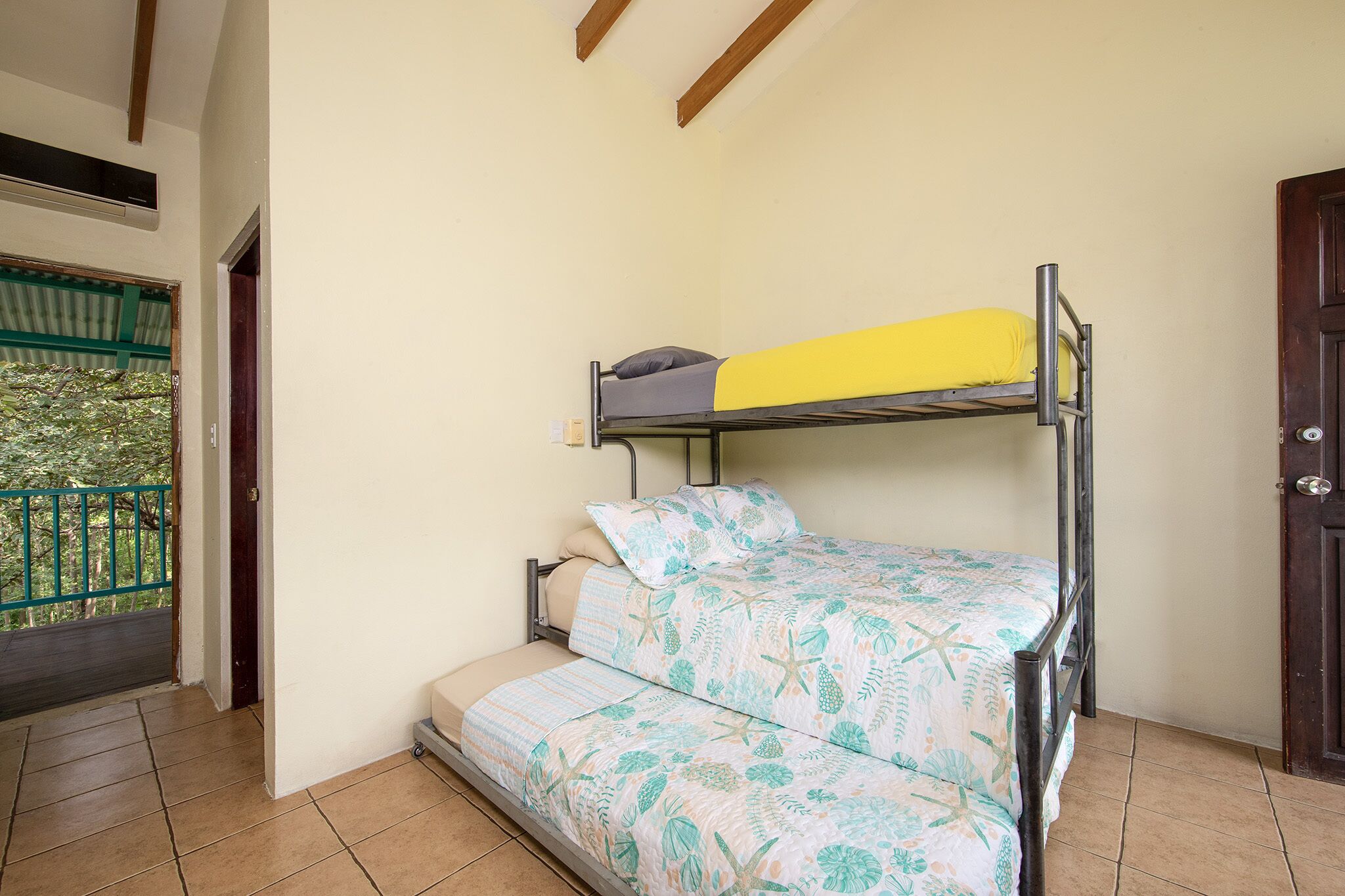 A room with a bunk bed, a small sofa, a door, and a balcony with a railing.