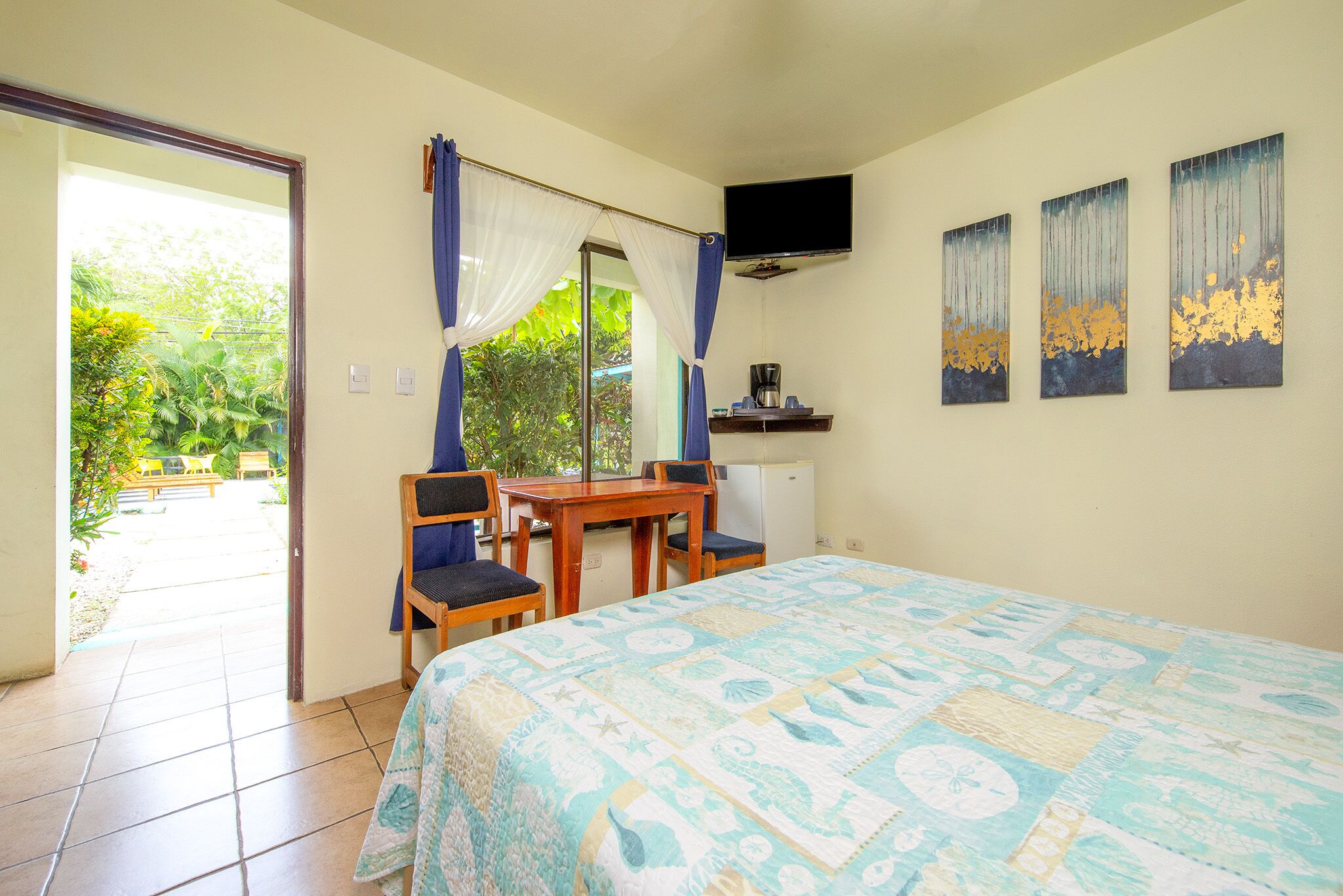 Un dormitorio con cama, escritorio, sillas, televisión y vistas al exterior.