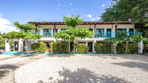 Un edificio de dos pisos con un patio de grava, un banco y un árbol en el centro.