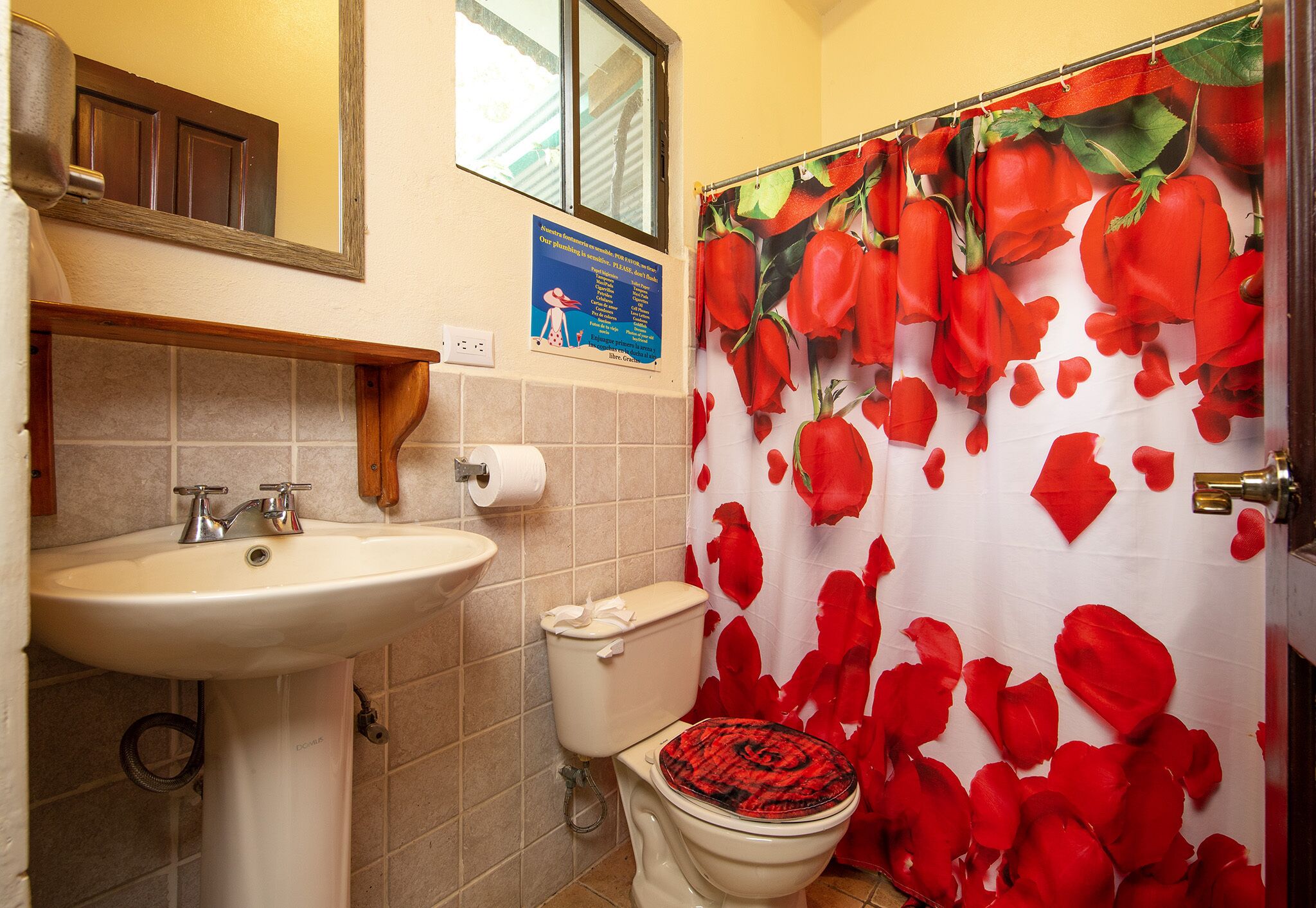 Un baño con lavabo, inodoro y cortina de ducha con estampado de rosas.