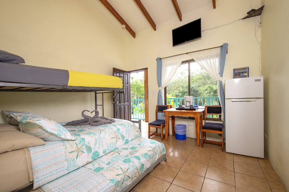 A small, cozy room with a bunk bed, a kitchenette, a table with chairs, and a refrigerator.