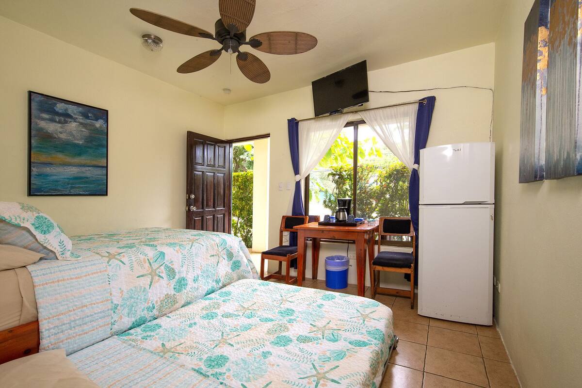 A bedroom with two beds, a ceiling fan, a TV, a refrigerator, and a window with curtains.