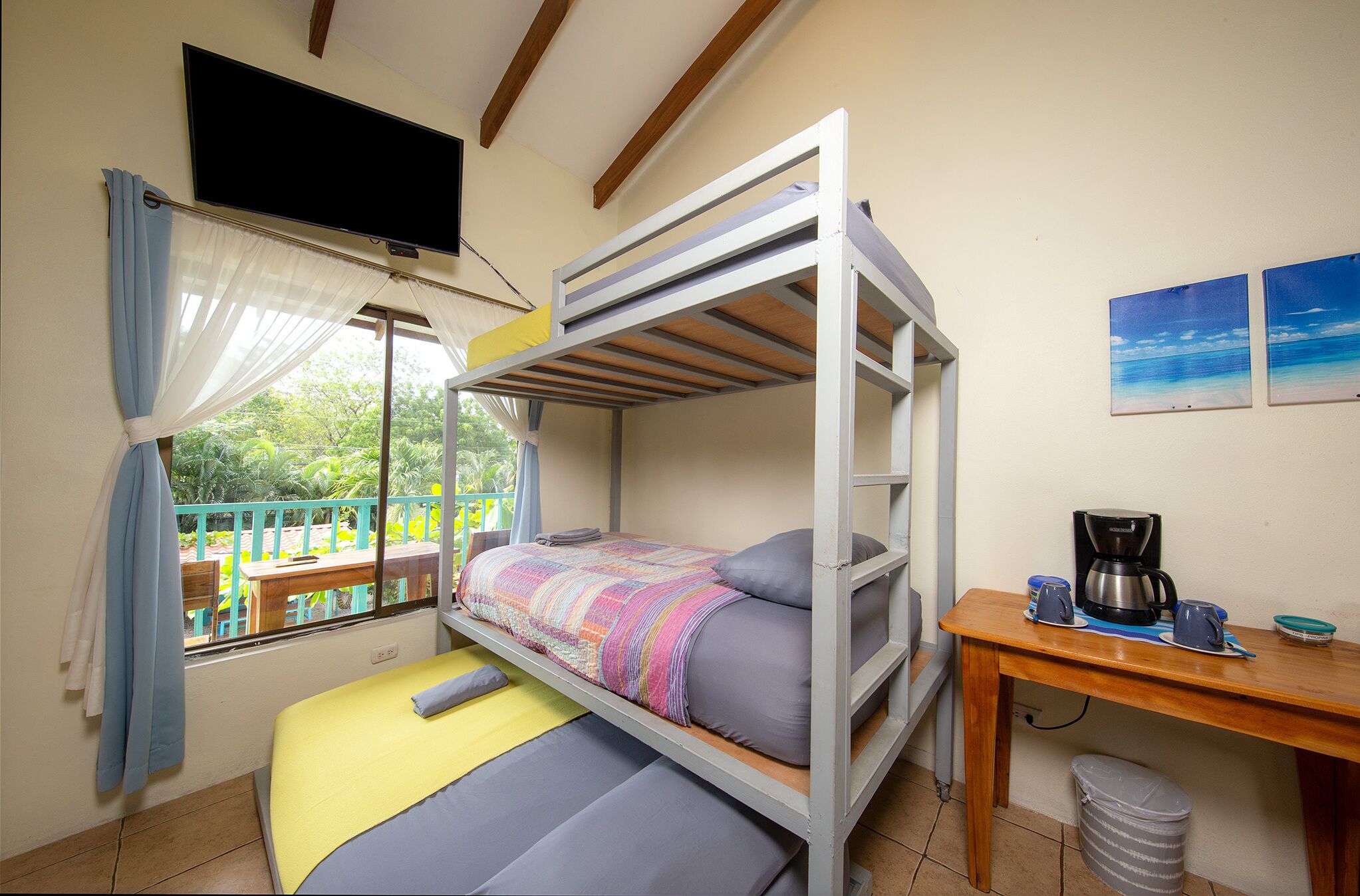 Quarto com beliche, janela, mesa com cafeteira e televisão na parede.