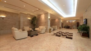 A spacious lobby with marble flooring, multiple seating areas, a checkered rug, and a large plant. - Snood Al Aziziah (Makkah)