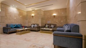 A spacious living area with three sofas and two coffee tables, marble walls, and wall-mounted lighting. - Snood Al Aziziah (Makkah)
