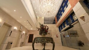 A lobby with a chandelier, a decorative table, and a clock on the wall. - Snood Al Aziziah (Makkah)
