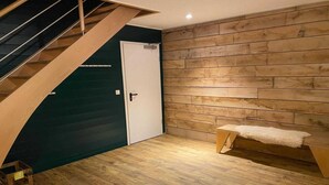 Une pièce avec un plancher en bois, un banc, une porte et un escalier.