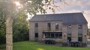Une maison moderne à deux étages, dotée d’un toit en pente, de grandes fenêtres et d’un patio couvert aménagé avec du mobilier d’extérieur.