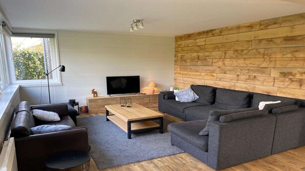 Un salon moderne avec un canapé gris, une table basse en bois et un téléviseur placé contre un mur en bois.
