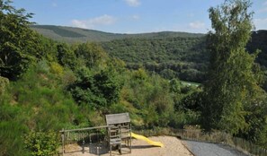 Explore the playground area surrounded by lush greenery and hills, featuring a play structure and slide.