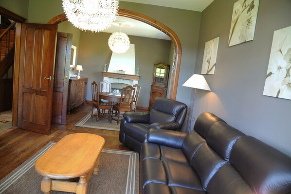 A living room with a leather sofa, wooden bench, and a dining area with a chandelier.